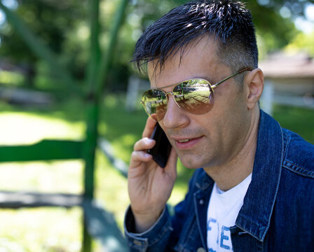 Smiling man with sunglasses talking on phone in park