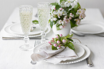 Beautiful table decor for a wedding dinner with a spring blooming apple tree flowers. Celebration of a special event. Fancy white plates, wineglasses