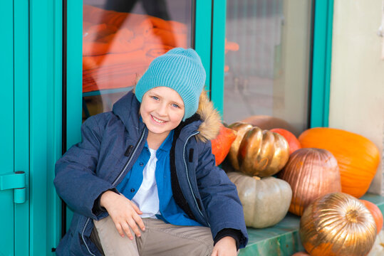 boy in a jacket sitting on the step  near pumpkins, thanksgiving decorations in front of the entrance