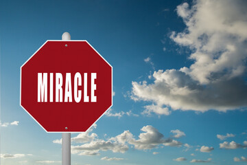 Red stop sign with the word Miracle on a blue sky background.