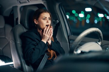 an emotional, frightened woman is sitting behind the wheel of a car in a black shirt, wearing a seat belt, expressing her emotions, covering her face with her hands. Photography at night 