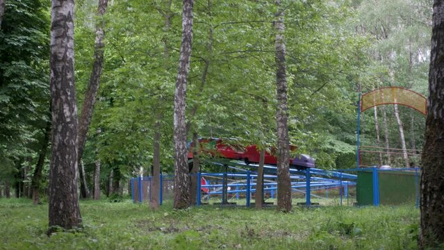 People riding on an old half-empty authentic soviet rollercoaster in local park. Friedns enjoy their free time in amusement park on a small wagon ride. Dated Eastern European theme park attraction 
