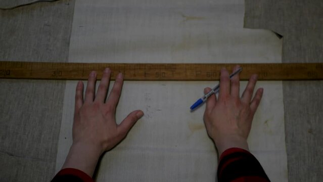 POV of white female seamstress measuring curves on cloth with a large wooden ruler and marking lines with a pen. Feminine caucasian hands estimating the size of sewing parts for future clothes 
