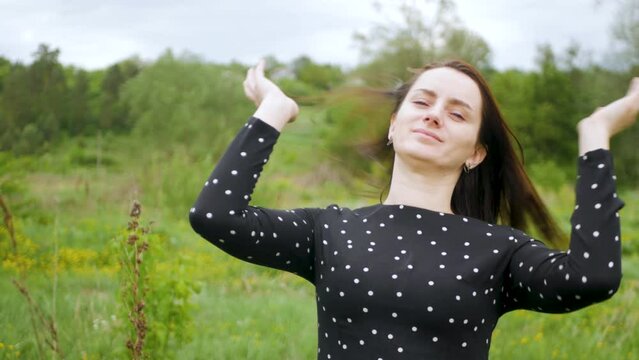 Attractive young woman grooming and brushing hair in a beautiful grassy meadow. Gorgeous caucasian female playing with long brown hair outdoors. Charming lady in black dress fixing hair before shoot
