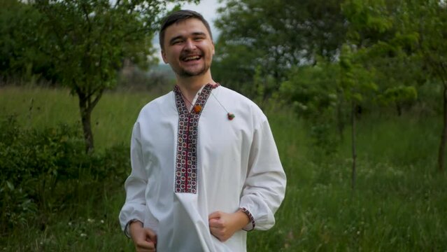 Happy caucasian man in traditional Eastern European embroidered shirt celebrating and cheering. Beaming bearded guy in conventional vyshyvanka rejoicing and clenching fists due to victory and success
