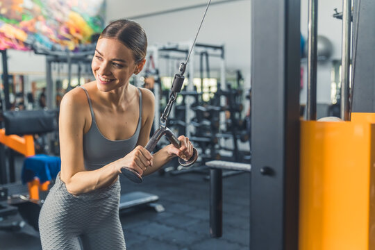 Indoor gym shot of a skinny caucasian young adult woman with slicked back hair trying out professional gym equipment for the first time. Arms exercises. High quality photo