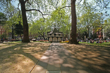 Soho Square in London on a sunny day with people relaxing and sunbathing.