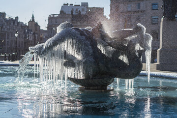 Frozen fountain statues of Trafalgar Square in London. Icicles mystically hanging off bronze water fountain