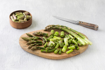 Wooden board with chopped asparagus on a light grey 
background. Cooking homemade food