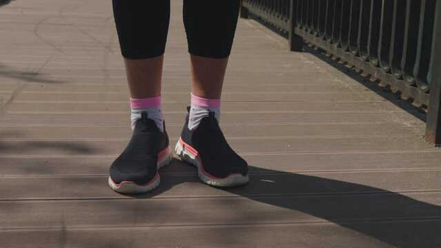 legs in black pink snickers warming up on wooden path in park, feet rotation exercises, close-up. concept of healthy lifestyle, sport outdoors, working out fresh air, steps nft finances, money concept
