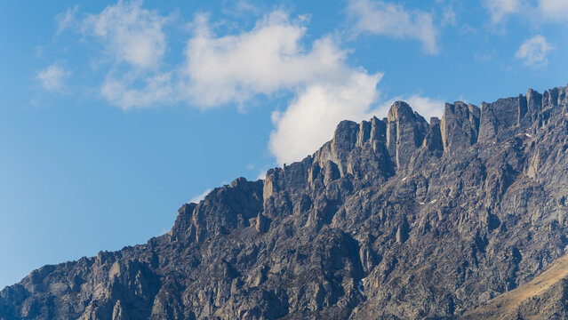 Contrast between blue sky with white clouds and rocky black mountain. High quality photo