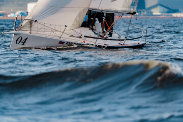 Teamwork in sailing regatta at sunset, sailing yacht in roll, big waves, hot racing