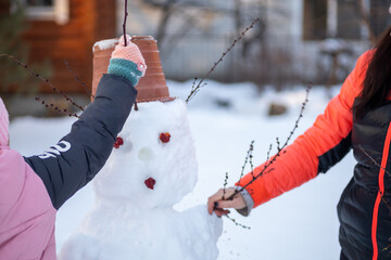 Close up of little girl and mother hands making snowman together on backyard in daytime while...