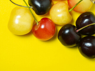 Sweet cherry with a stem on a yellow background.   Natural berries on the table. Harvest. Cherries of different varieties. Place for an inscription