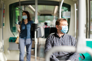 Adult man wearing medical mask and rubber gloves riding city bus on way to work in sunny spring...
