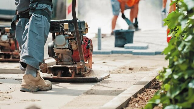 Roadworks Construction Worker Using Ground Plate Compactor Preparing Surface for Laying Sidewalk Pavement Flagstones
