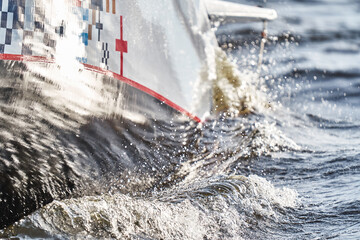 water shatters against the glossy side of a sailing boat in a roll at sunset, splashes of water and...
