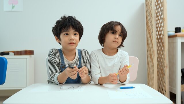 Happy asian two boy kids creatively draw and talk with brushes and crayon on the table. Little boy kindergarten preschool student in class.First time to school education,Childhood education concept.