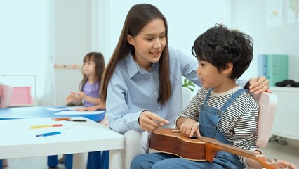 Obraz premium Young asian teacher teaching guitar and ukulele to his little boy.Little boy learning guitar at kindergarten.Close up,Ukulele class at school. Child learning guitar from her teacher.Musical education.