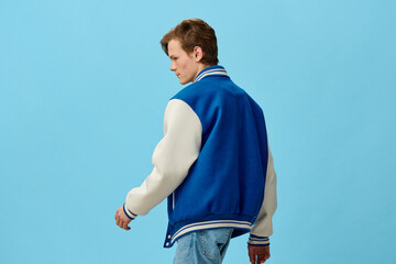a handsome, young man student in a trendy blue bomber jacket stands with his back to the camera on...