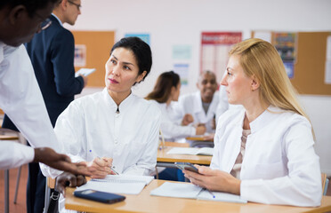 Adult people in white lab coats working in small groups during professional training course, discussing task set by teacher