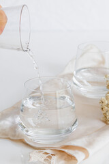 Person taking a jug of water to pour with a glass. Glass cup containing natural water on white background. Minimalist image. Drinking water simplicity concept.