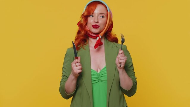 Ready to eat. Hungry redhead young woman in green jacket and dress waiting for serving dinner dishes with cutlery, will appreciate delicious restaurant meal. Ginger girl isolated on yellow background