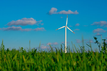 Wind generator in green grass.Green energy. Windmill on blue sky background.Environmentally friendly natural energy source.Consumption of natural energy.