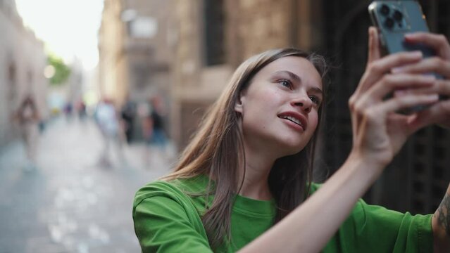 Positive blonde woman wearing green t-shirt making photo of the street by phone outdoors