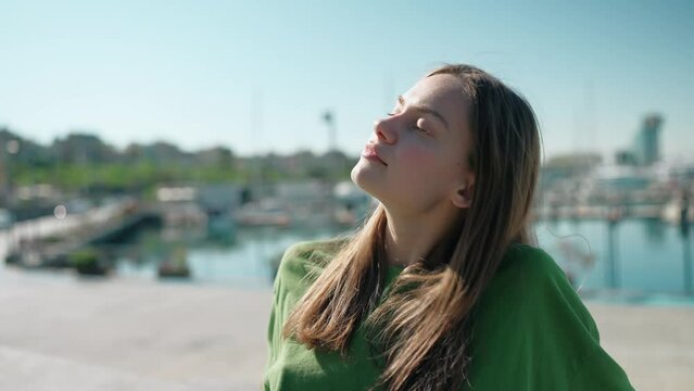 Pleased blonde woman wearing green t-shirt sitting with closed eyes on the seafront near yachts outdoors