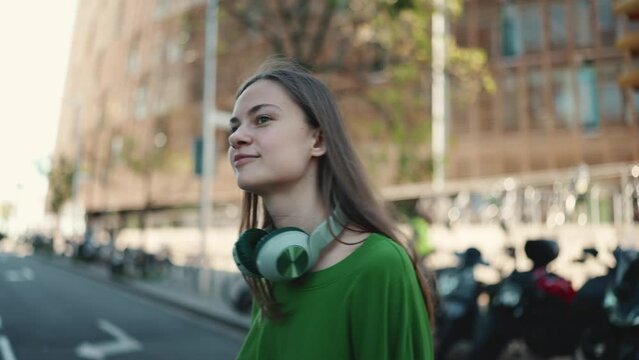 Handsome blonde woman in headphones wearing green t-shirt walking outdoors