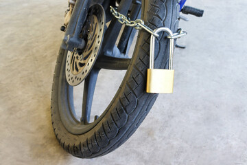 Metal padlock with steel chain tied to front wheel of motorcycle for safety locked up.
