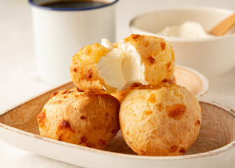 Minas Gerais cheese bread, hot, with a cup of black coffee and cream cheese, on a white tablecloth, copy space