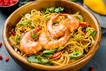 wok with shrimp, egg noodles with shrimps and vegetables on wooden bowl macro close up
