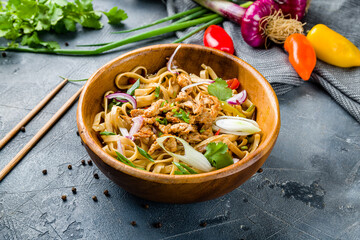 Udon noodles with chicken and vegetables on wooden bowl on grey table