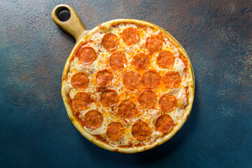 Pepperoni pizza on wooden board on blue concrete table top view