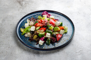 Greek salad with feta cheese and vegetables on blue plate on grey table