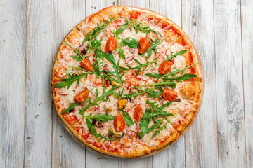 Pizza with seafood and aragula with tomatoes and cheese top view on white wooden table