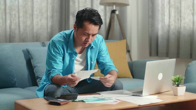 Asian Man With A Laptop Looking At The Bill And Crumpling It Then Throw It Away
