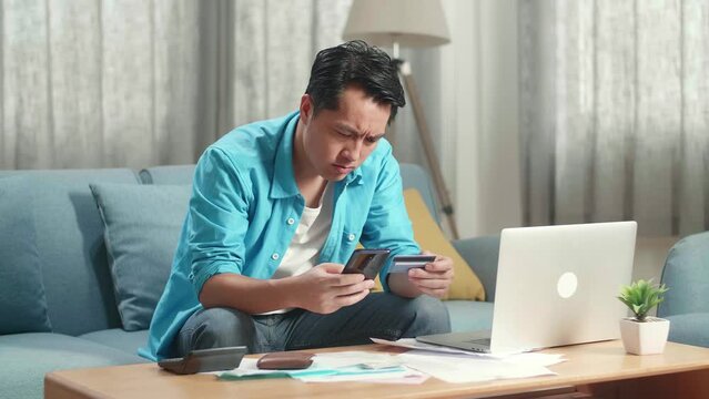 Asian Man With A Laptop Holding Credit Card And Smartphone Shaking His Head Due To Unable Pay Money
