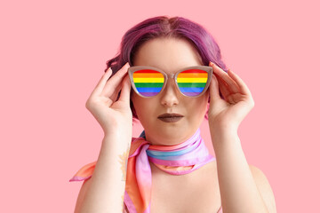 Beautiful young woman with stylish rainbow sunglasses on pink background. Concept of LGBT