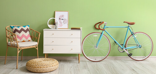 Interior of stylish room with armchair, chest of drawers and bicycle near green wall