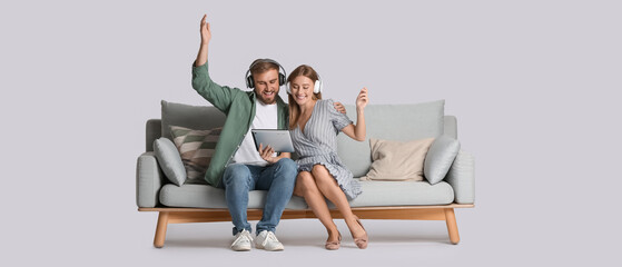 Happy young couple with tablet computer listening to music while sitting on sofa against light background