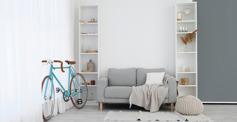 Interior of light living room with bicycle, grey sofa and shelving units