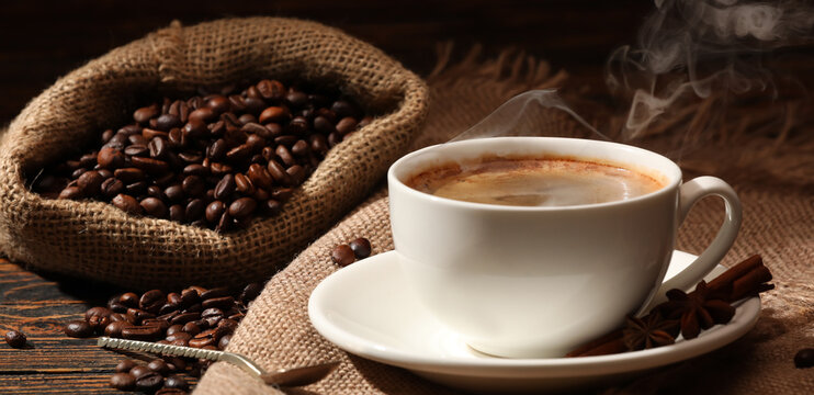 Cup of hot coffee and bag with beans on wooden background