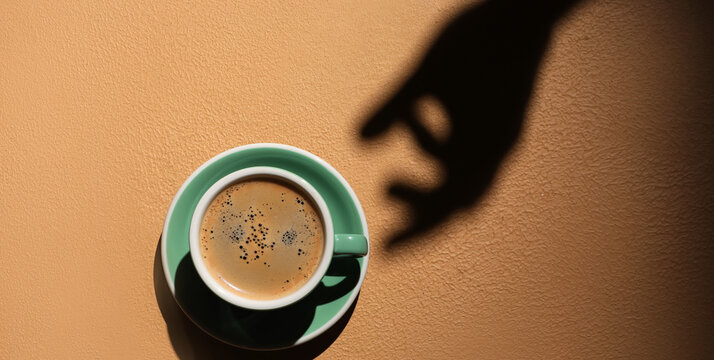 Shadow of hand and cup with hot coffee on color background, top view