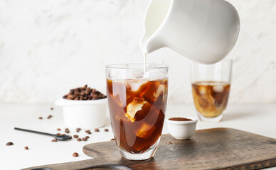 Milk pouring into glass with cold brew coffee on light background - obrazy, fototapety, plakaty