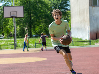 Obraz premium Cute young teenager in green t shirt with a ball plays basketball on court. Sports, hobby, active lifestyle for boys