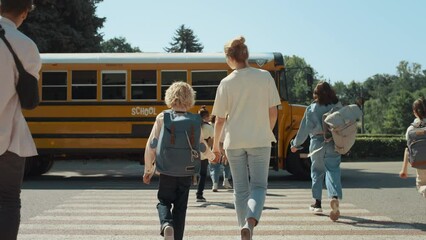 Mother hold hand schoolboy walking to bus. Energetic pupils running crossway.