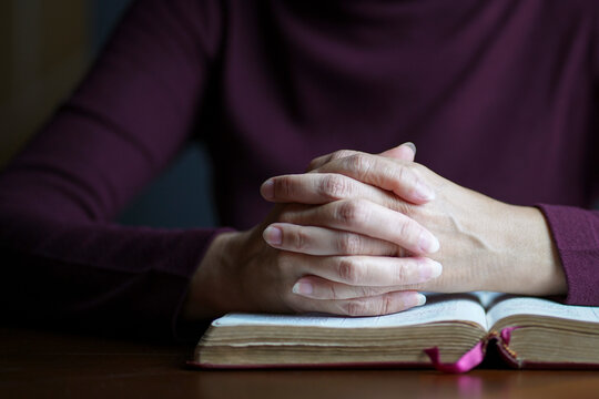 Woman hands in prayer posture on top of open bible. Copy space.